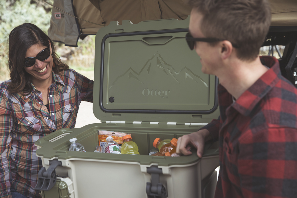 Two people stand beside an open venture cooler full of drinks.