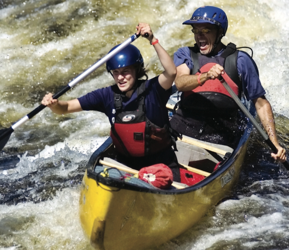 Man and woman paddle through whitewater in a Mad River Caption canoe