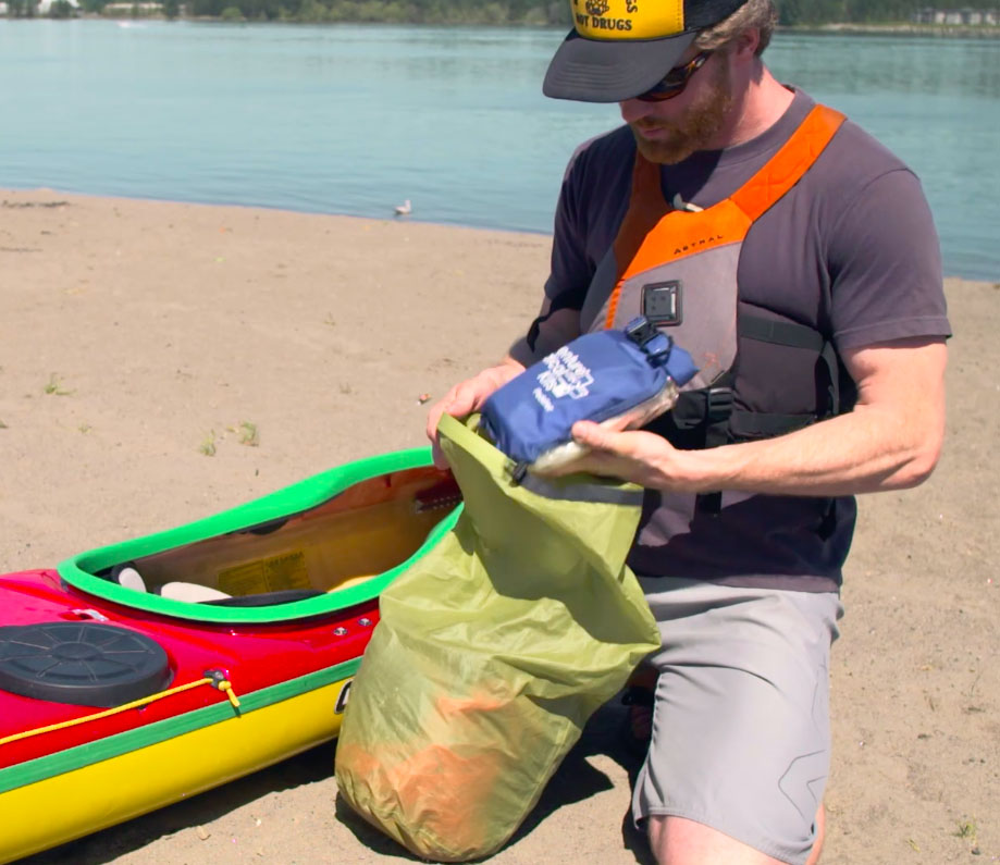 A paddler fills a dry bag with extra clothes.