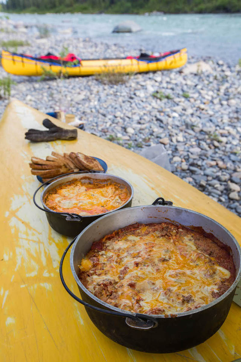 Lasagna cooks in a dutch oven at a canoe campsite. 