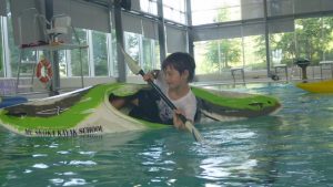 A child edges his kayak in a pool as he prepares to roll a kayak.
