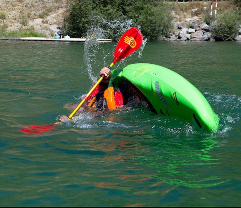 A whitewater kayaker in a green boat rolls from upside down. 