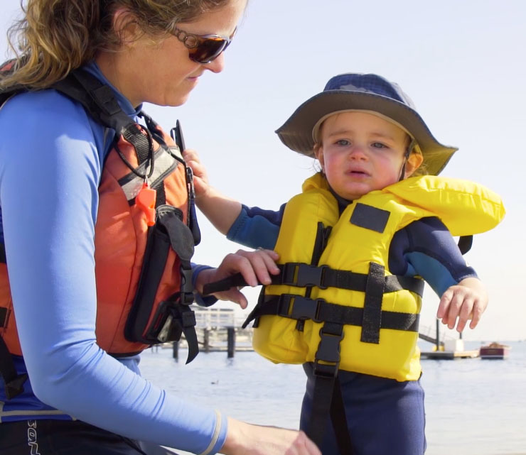 A mother makes sure her child is safely buckled into their lifejacket.