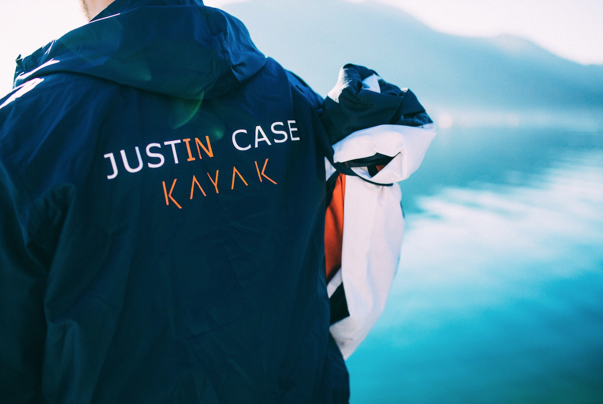 A man stand on the waters edge with a Justin Case Kayak bag over his shoulder