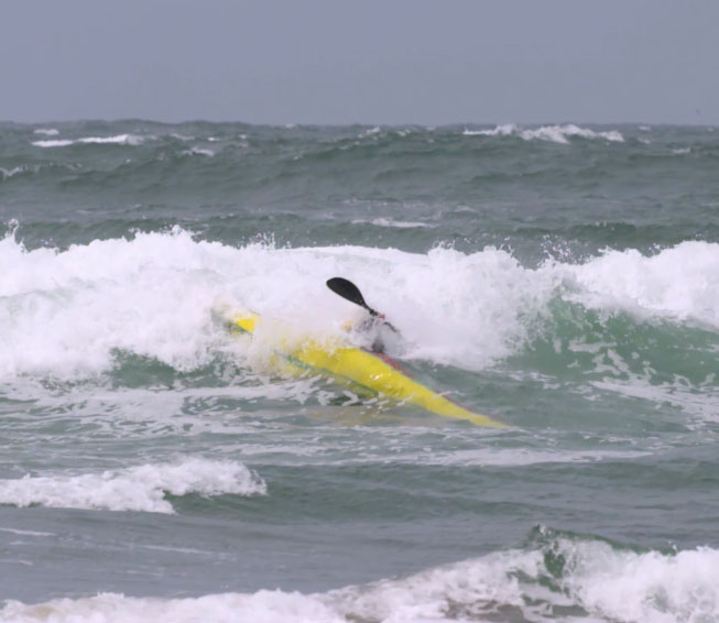A paddler flipping a kayak in harsh weather.