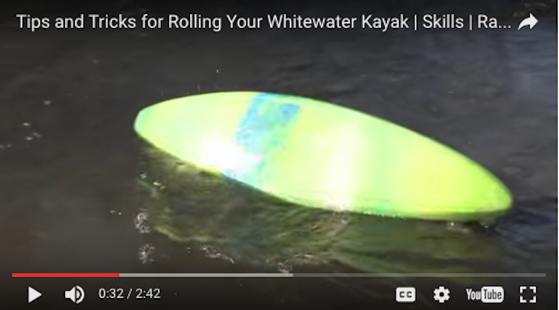 A screenshot of a video showing a whitewater kayaker rolling their green kayak. 