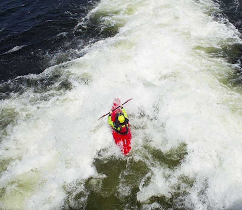 A whitewater kayaker in a red boat is shot from above. 