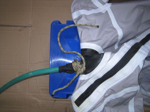 A hose is tied to the neck gasket of a drysuit to fill it with water for a leak test