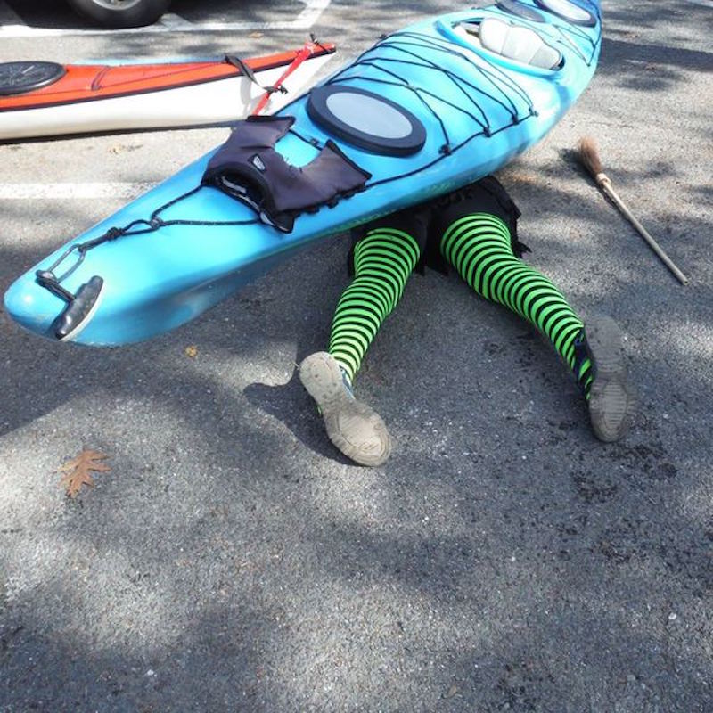 A woman in green striped stockings under a kayak
