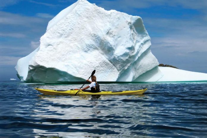 woman sea kayaking beside an iceberg