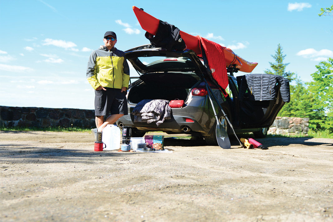 man standing next to his hatchback surrounded by paddling gear