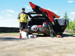 man standing next to his hatchback surrounded by paddling gear