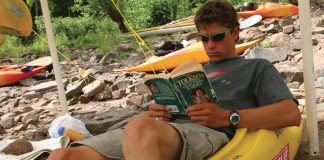 man sitting in kayak reading Fellowship of the ring