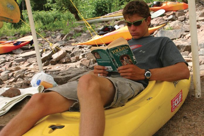 man sitting in kayak reading Fellowship of the ring