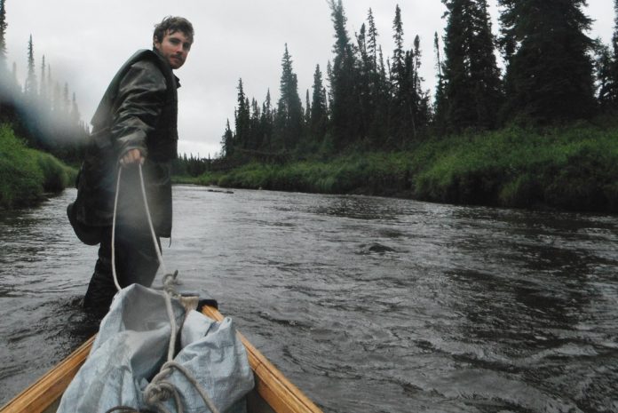 man pulling canoe behind him standing in a river