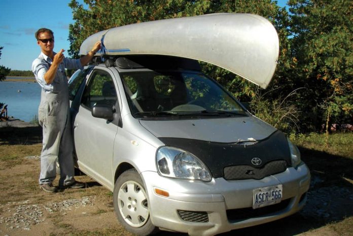 man standing next to his car with a canoe strapped on top