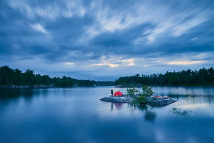 man on a small island with a tent and sea kayak on a lake