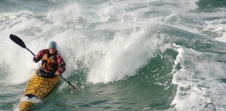 woman in sea kayak surfing a wave