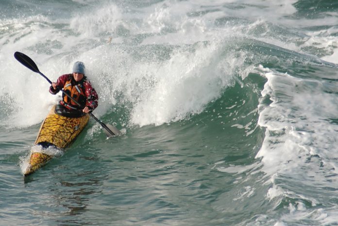 woman in sea kayak surfing a wave
