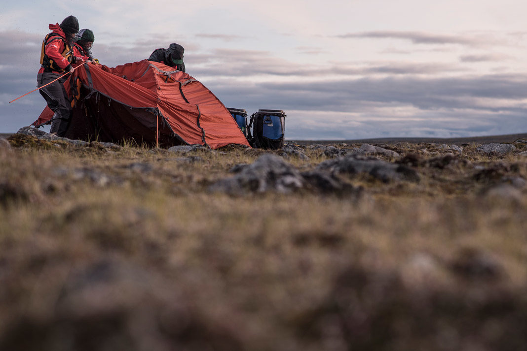 three people setting up a tent in vast territory