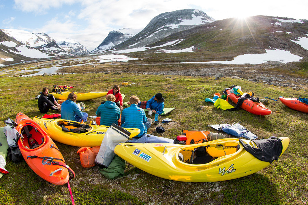 several paddlers surrounded by kayaks with mountains in the background