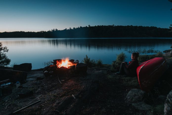 woman sitting against a canoe in front of fire