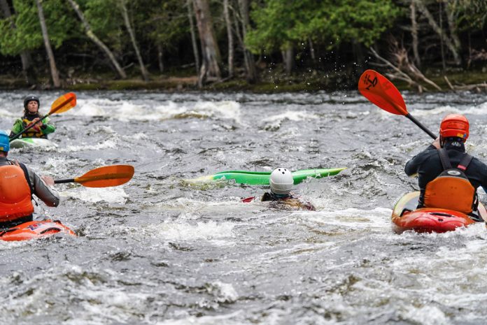 3 kayakers helping another kayaker who is swimming