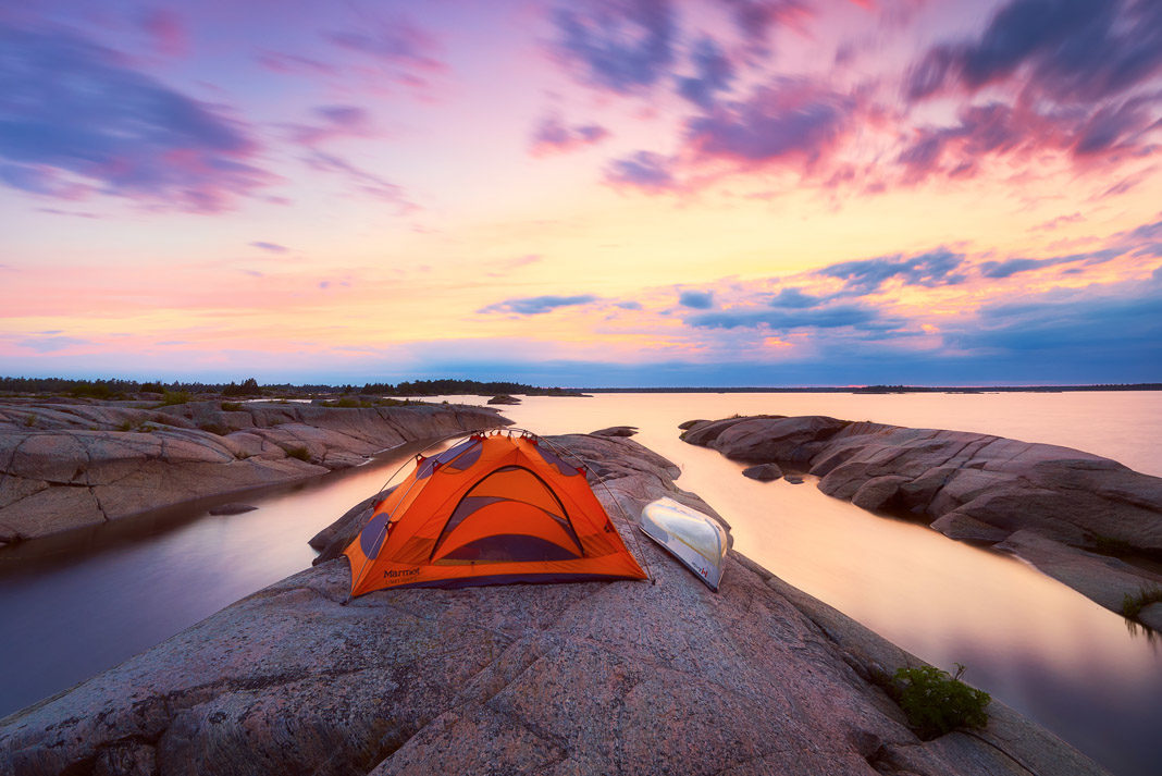 a tent and canoe on an island with a sunset in the background