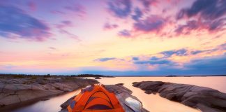 a tent and canoe on an island with a sunset in the background