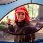 Canoe Camping With Kids: 7 Tips To Survive And Thrive Young boy stands outside a tent while canoe camping with kids