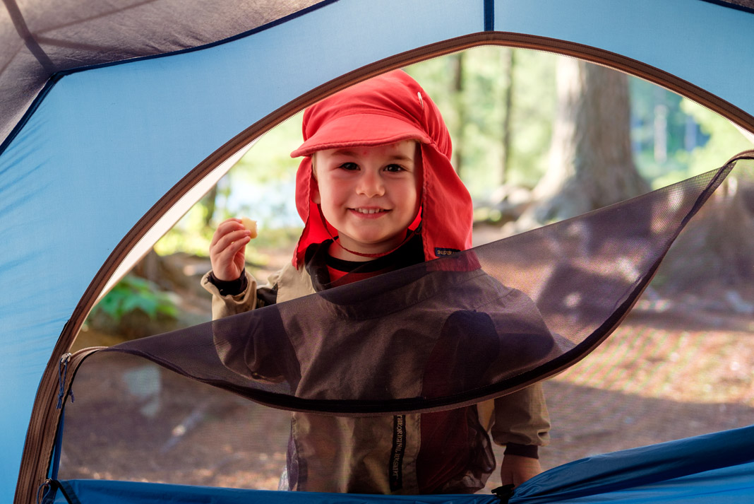 Young boy stands outside a tent while canoe camping with kids