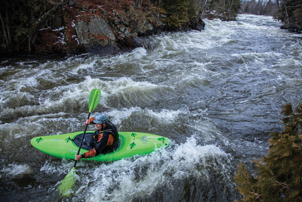 boater in a green kayak paddling through whitewater