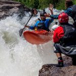 Why You Should Always Wear A PFD kayaker giving a high five to a friend on shore, all wearing PFDs