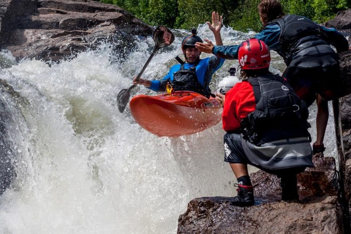 kayaker giving a high five to a friend on shore, all wearing PFDs