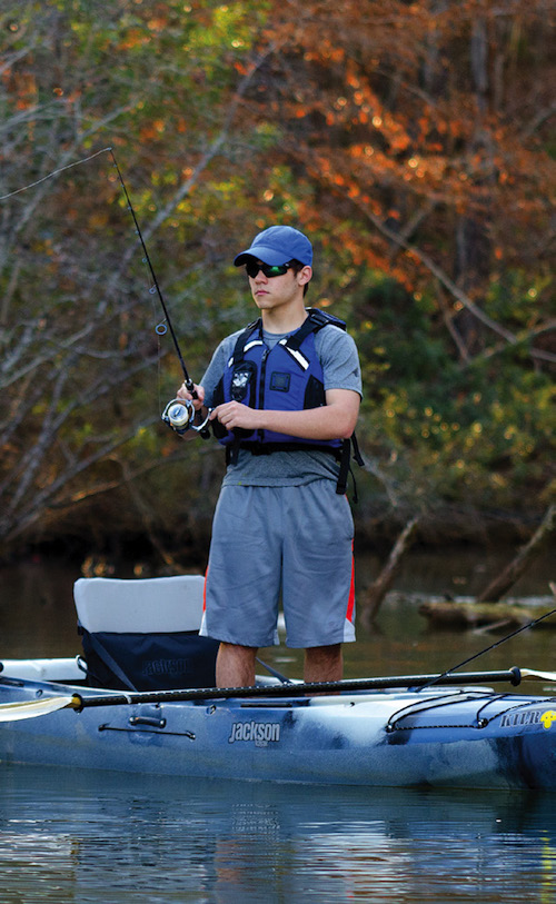 man stands and fishes from a sit-inside fishing kayak