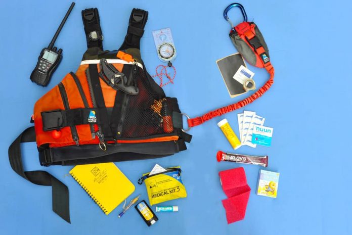 a PFD surrounded by safety gear such as a radio, a first aid kit, a whistel, sunscreen, a notepad and other gear to complete the kit.