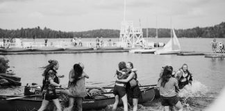 several young women hugging each other surrounded by canoes in Algonquin Park, Ontario.