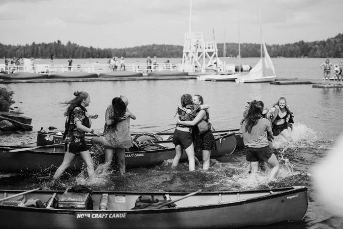 several young women hugging each other surrounded by canoes in Algonquin Park, Ontario.