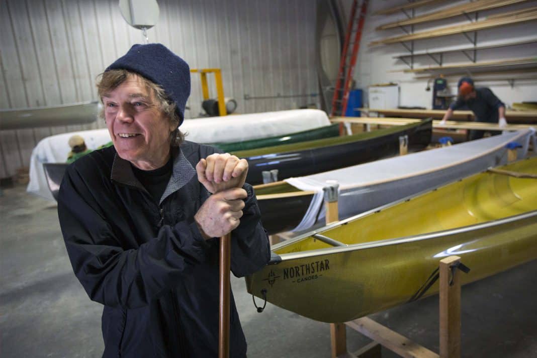 Explorer Will Steger smiling in front of his custom made canoes holding a canoe paddle