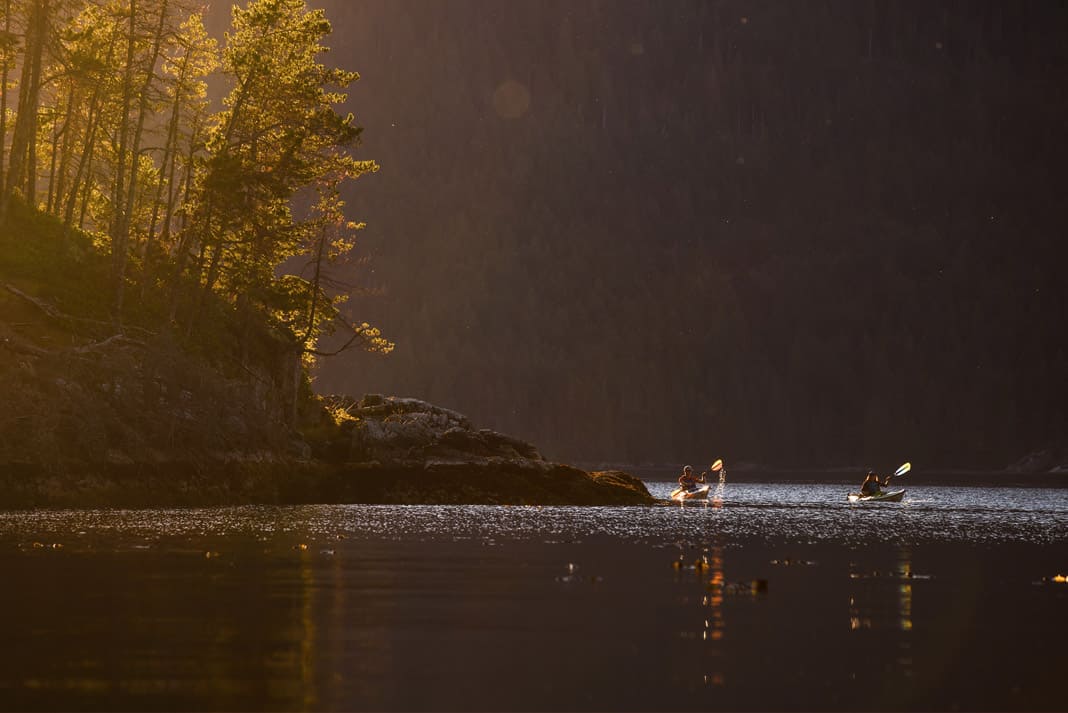 two kayakers coming around the corner of an island on a lake