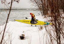 Man walking on snow carrying yellow kayak