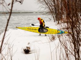 Man walking on snow carrying yellow kayak