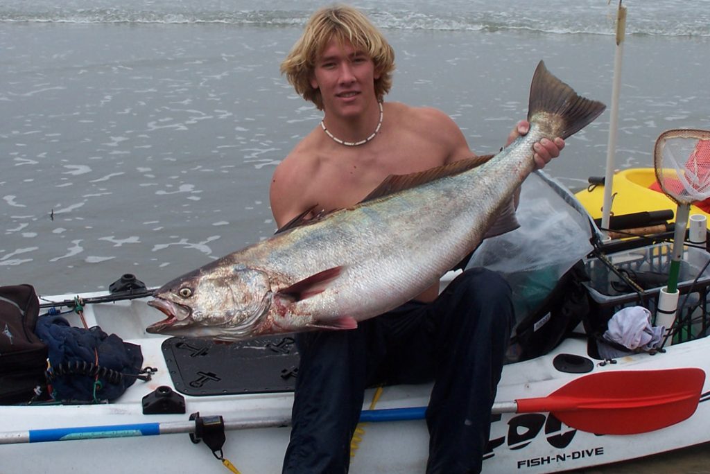 young man holding a large fish sitting in a cobra fishing kayak