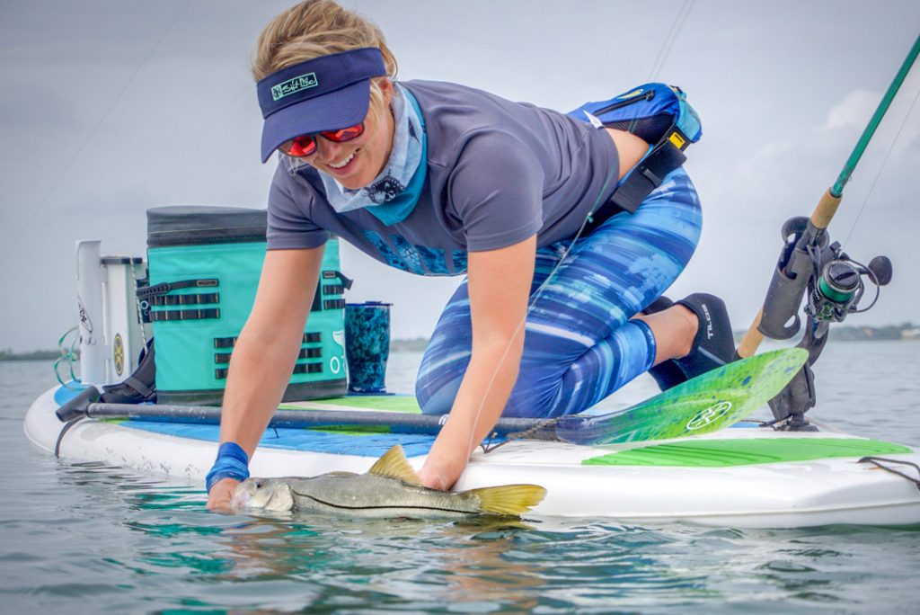 Bri Andrassy kneels on her paddleboard with a fish