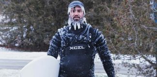 man standing with his paddleboard in the winter covered with icicles on his face