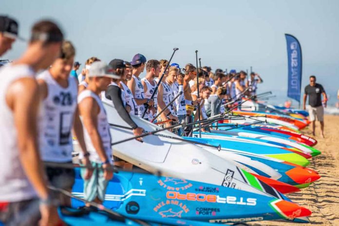 A group of standup paddleboard racers stand at the starting line