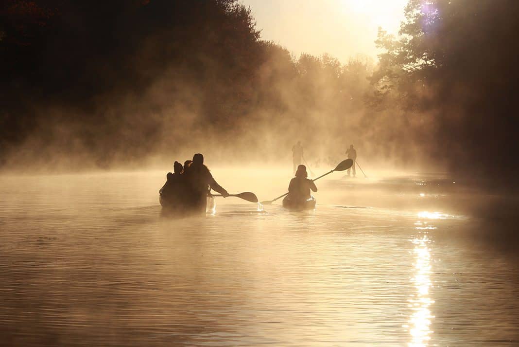 Canoeists paddle into a misty morning on the lake