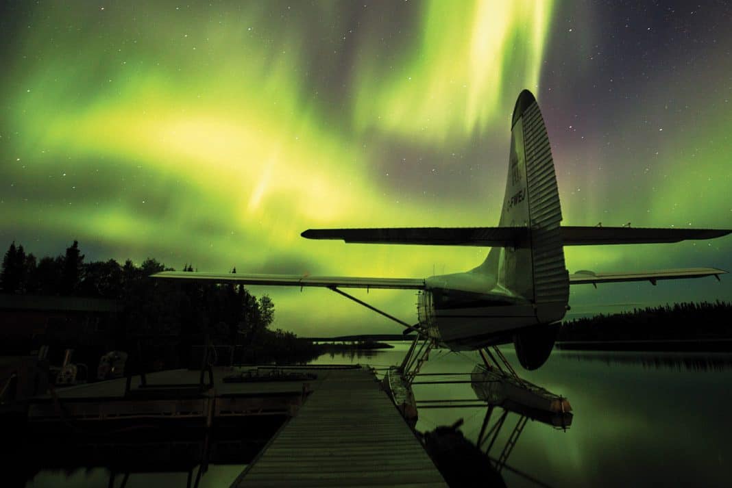 a seaplane docked with green northern lights in the sky