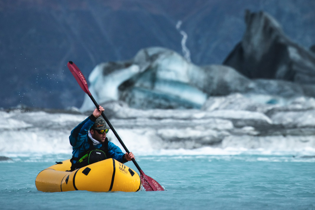 man paddling his inflatable kayak with stunning glaciers in the background