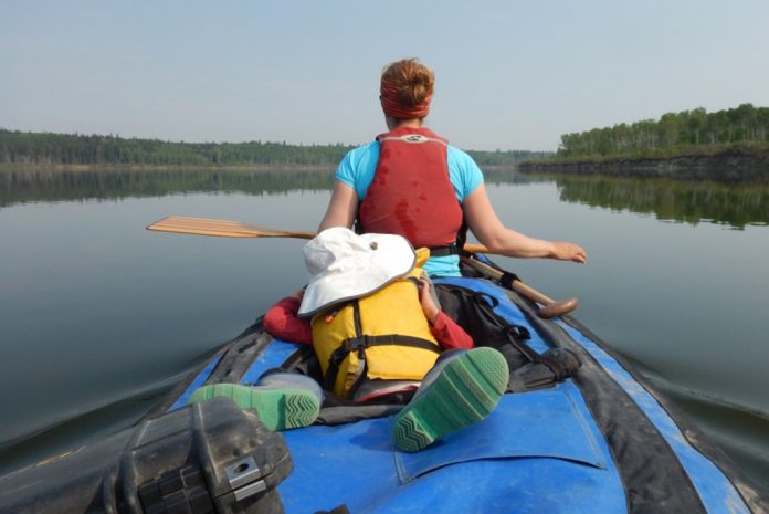 A child lies in a canoe while his mother paddles in the bow.